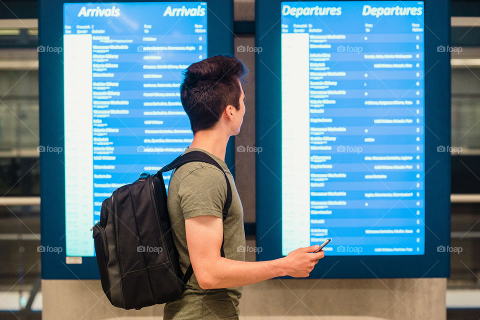 Young man standing in the railway station next to screens with schedule, planning a travel, travelling with backpack