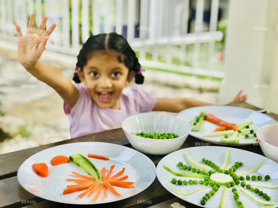 A 4 year old girl having fun in summertime by doing creative activities with vegetables as a sun and  trees .