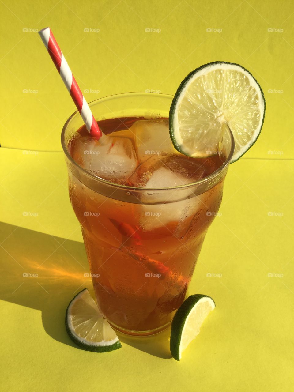 Cool, refreshing, freshly made, homemade, sweet iced tea with fresh green lime slices in a glass with a red and white straw sitting in the sunshine.