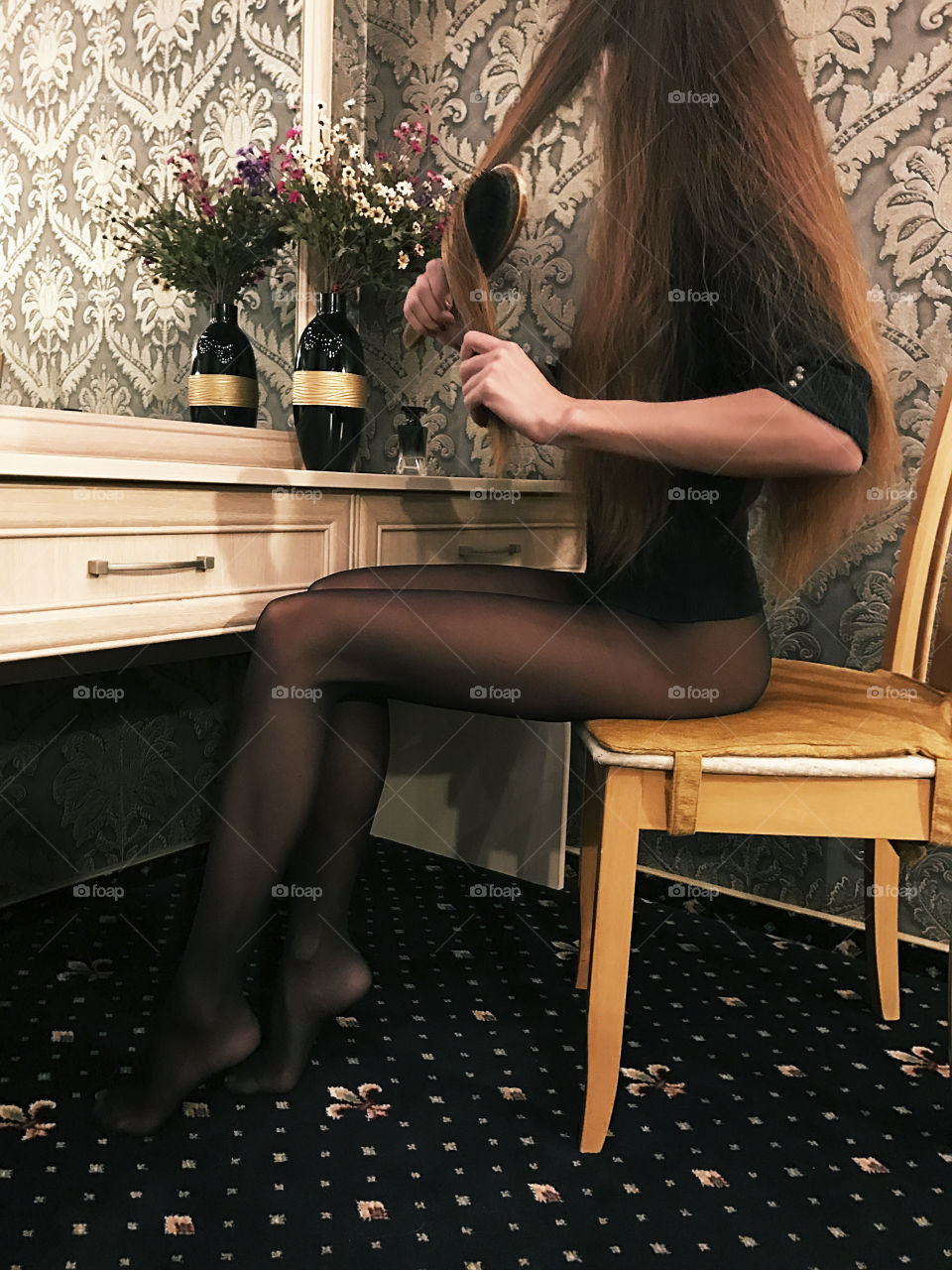 Young woman brushing her long hair in front of a mirror in bedroom before going out 