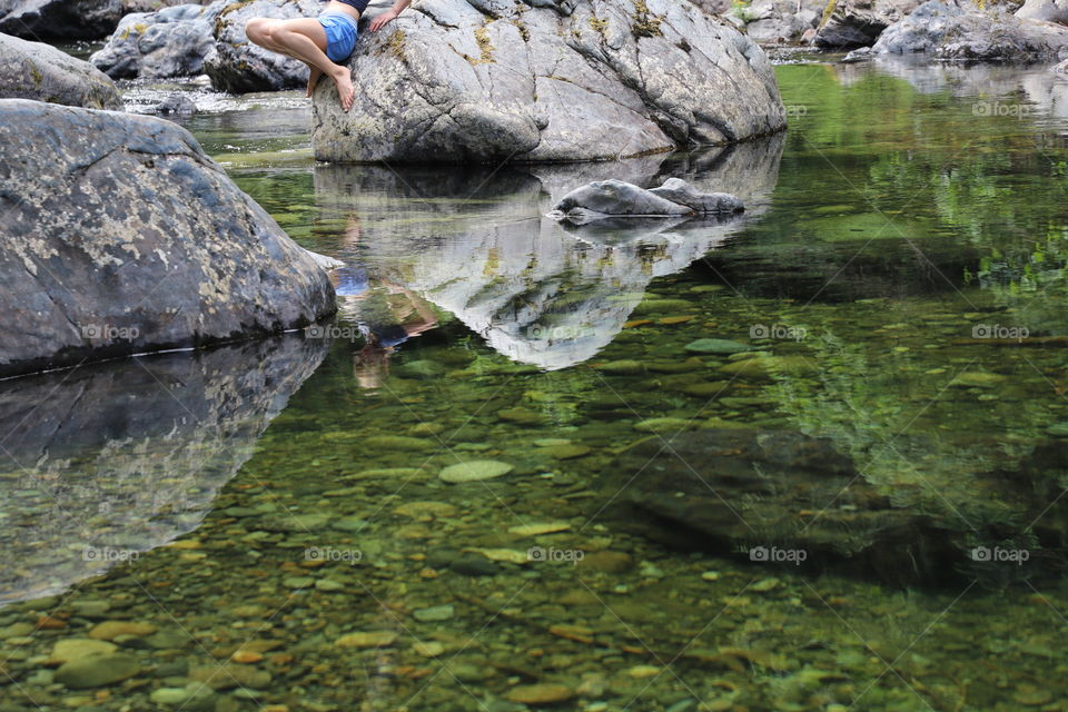 Girl intending to put her feet in the cool water while her body mirrors in the green river