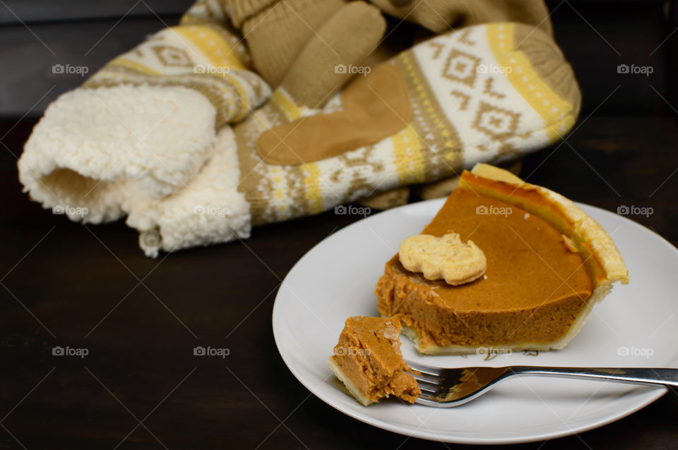 Autumn favorite dessert pumpkin pie on table next to warm mittens with heart shape 