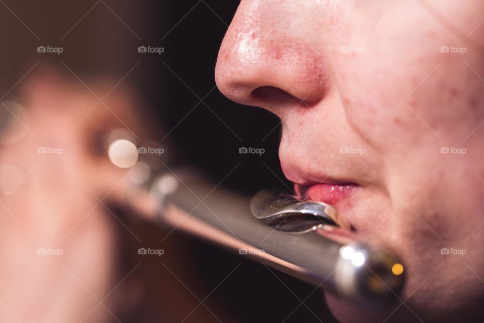A portrait of the lips of a flutist blowing into the mouth piece of a silver flute during a concert.
