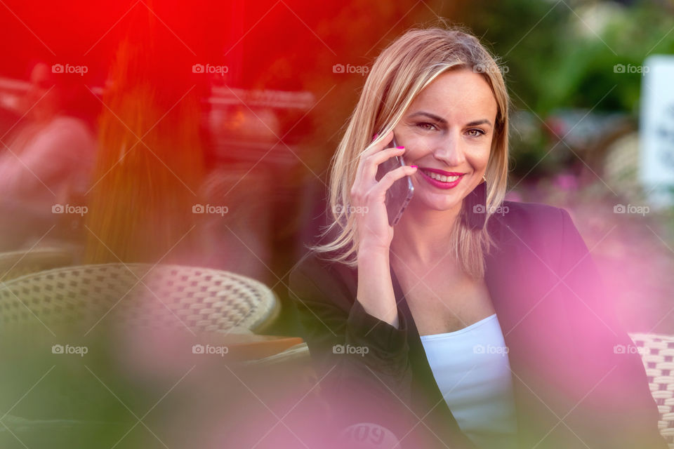 Blonde business woman talking on the phone in an outdoor cafe. The blurred foreground.