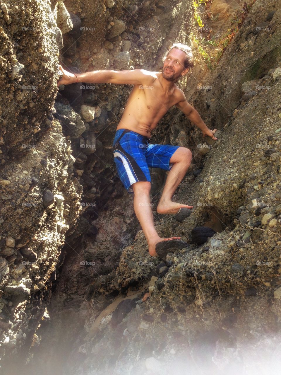 Shirtless man climbing rocky mountain