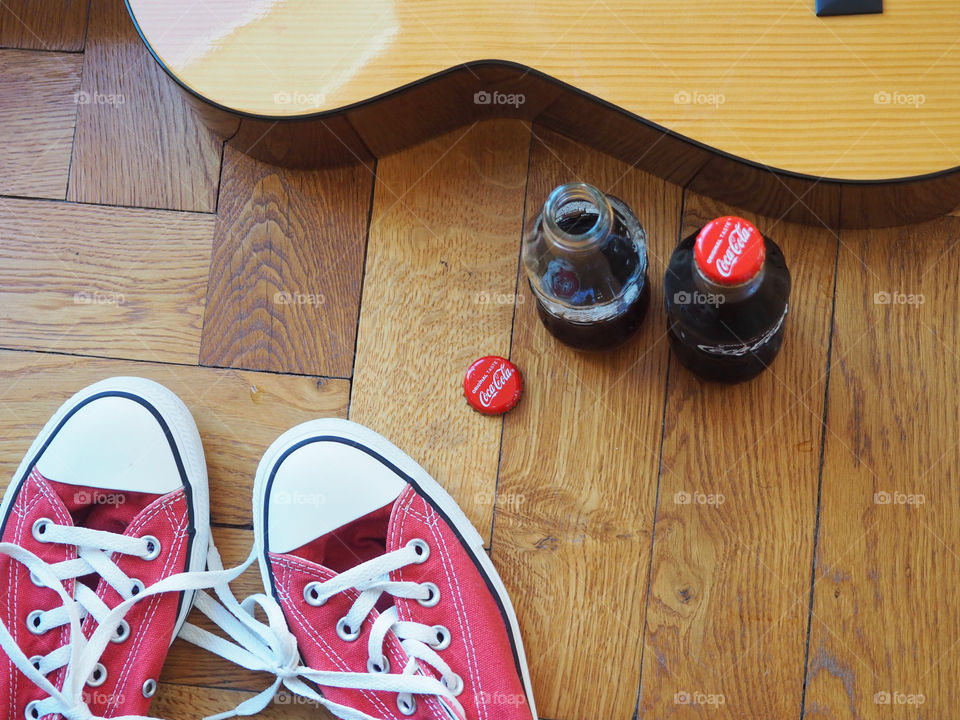 Coca Cola bottles on hardwood floor with red sneakers and guitar.