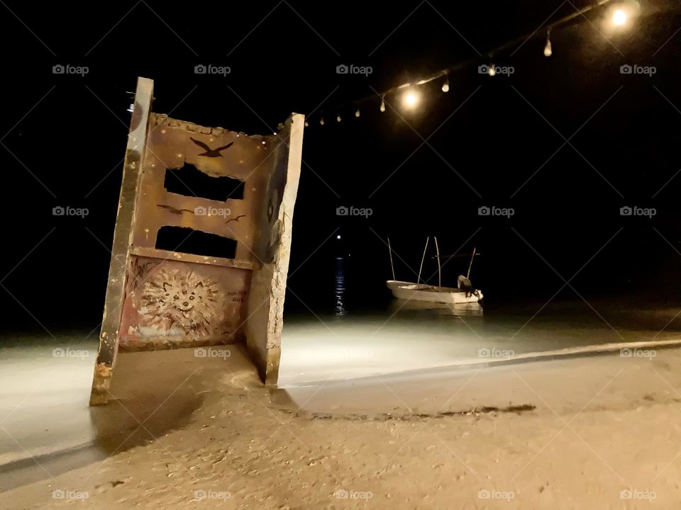 A cement structure filled with street art, a moored boat, the beach at night.