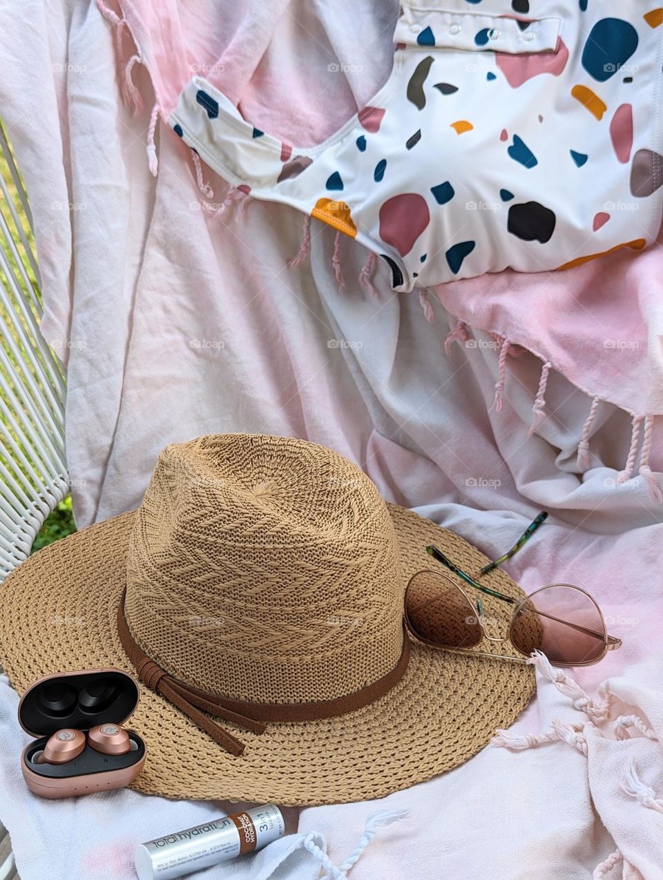 summer vacation packing essentials swimsuit Sun hat, aviator sunglasses, coconut hydration chapstick and pink tye dyed beach blanket