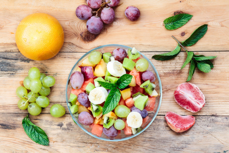 Making fruit salad with grapes, banana, grapefruit, kiwi and mint leaves