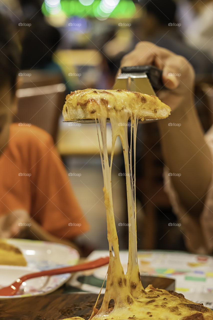 The hand holding Pizza with ham and cheese in spoon from the tray wood.