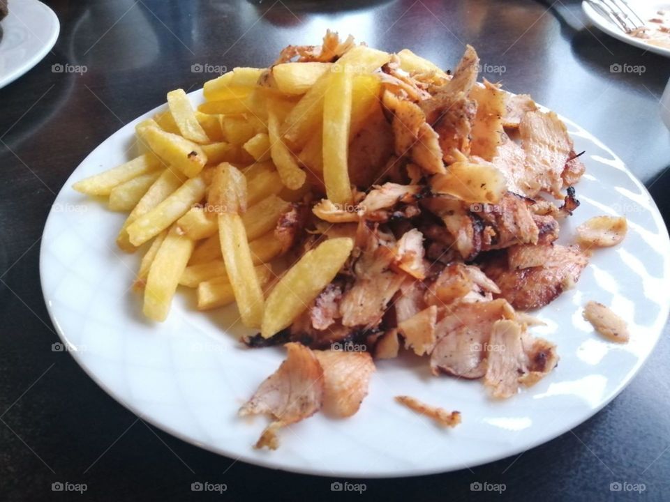 Fried potatoes with slices of meat on a white plate