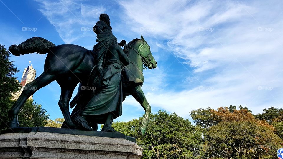 Statue of man and horse with blue skies and trees