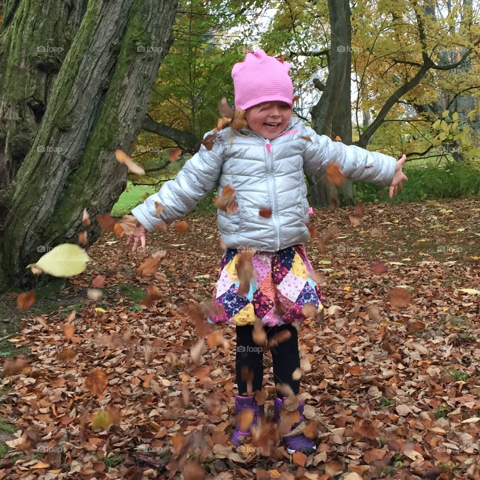 Small girl playing with autumn leaves