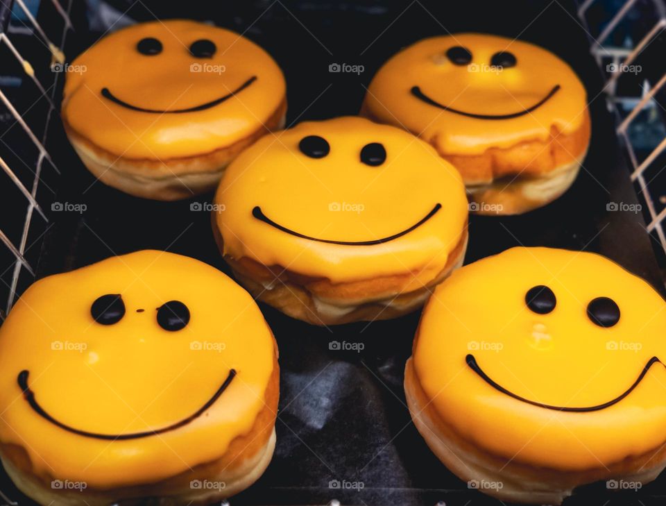 Beautiful tasty American donuts with yellow icing and chocolate smiley lie in a metal basket on the counter in the store, close-up side view.