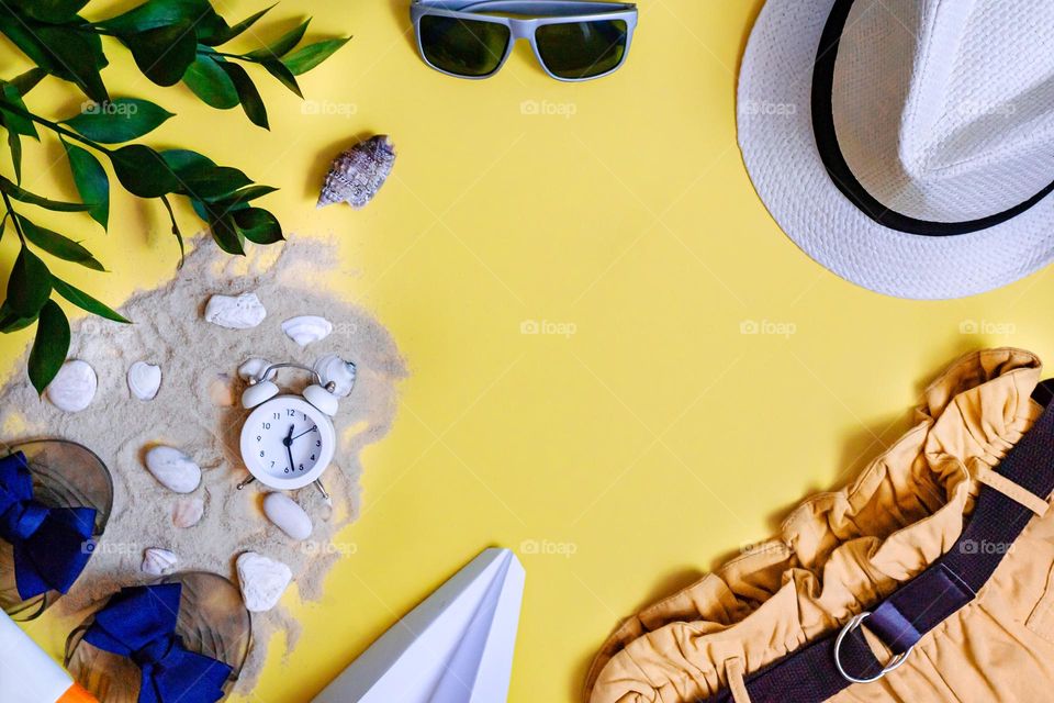 Flat lay on yellow background summer holiday accessories, sand, hat, shorts, glasses