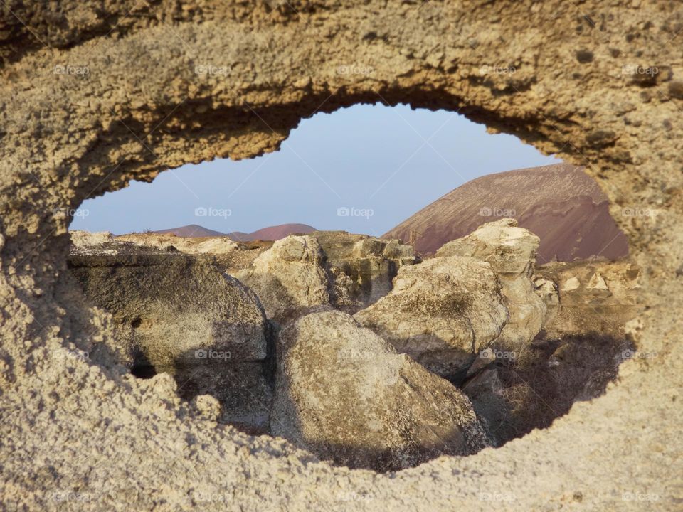 paisaje volcánico de piedras con fondo de montaña a la luz de el atardecer tomada desde un agujero de piedra