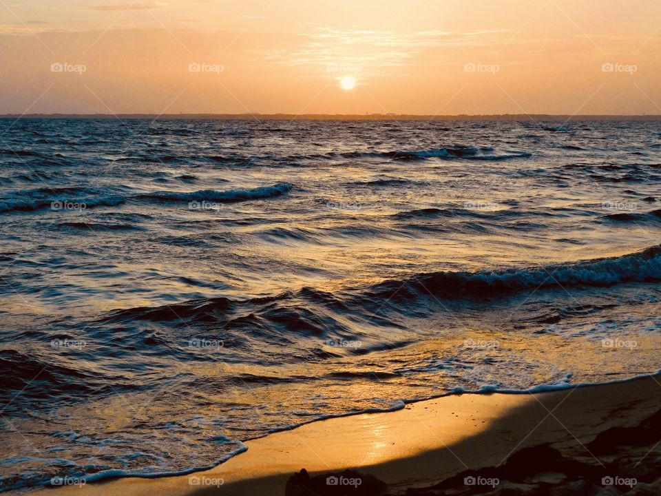 Ocean sunset - An orange haze from the setting sun reflects off the rolling waves, that crash upon the sandy shore