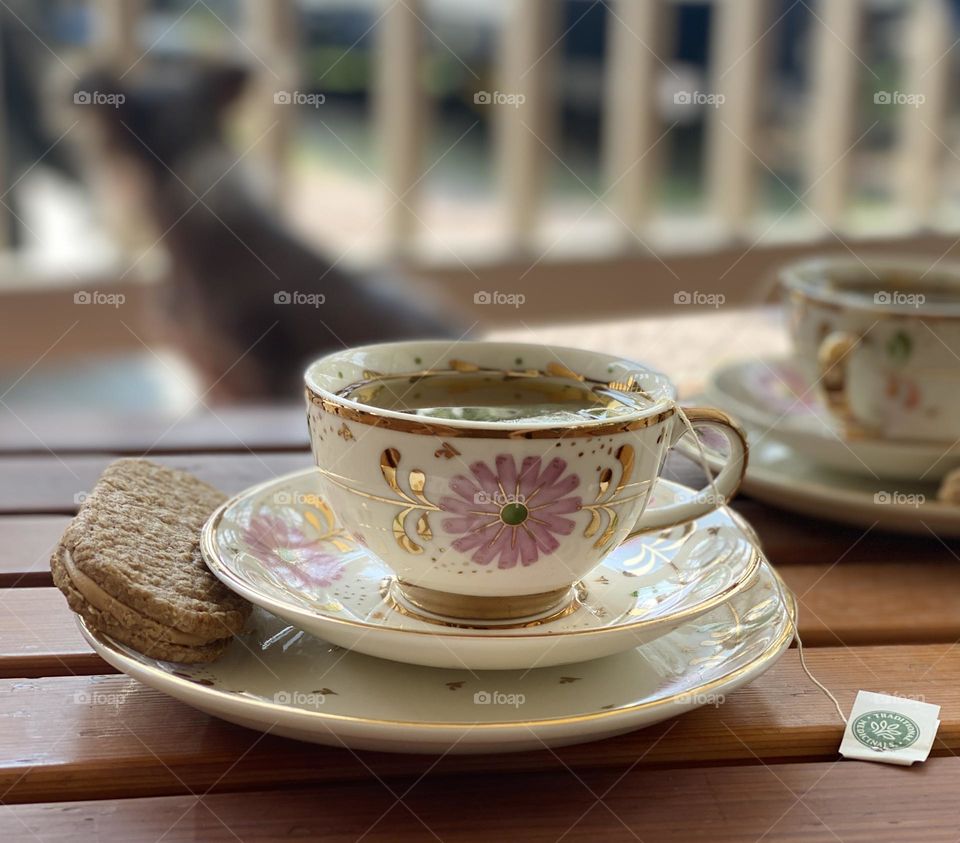 Tea cups with tea and biscuit inside on patio with dog in background 