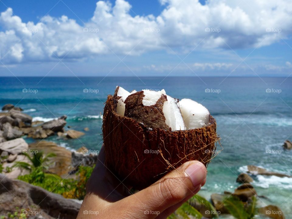 Hand with fresh coconut in front of Indian Ocean