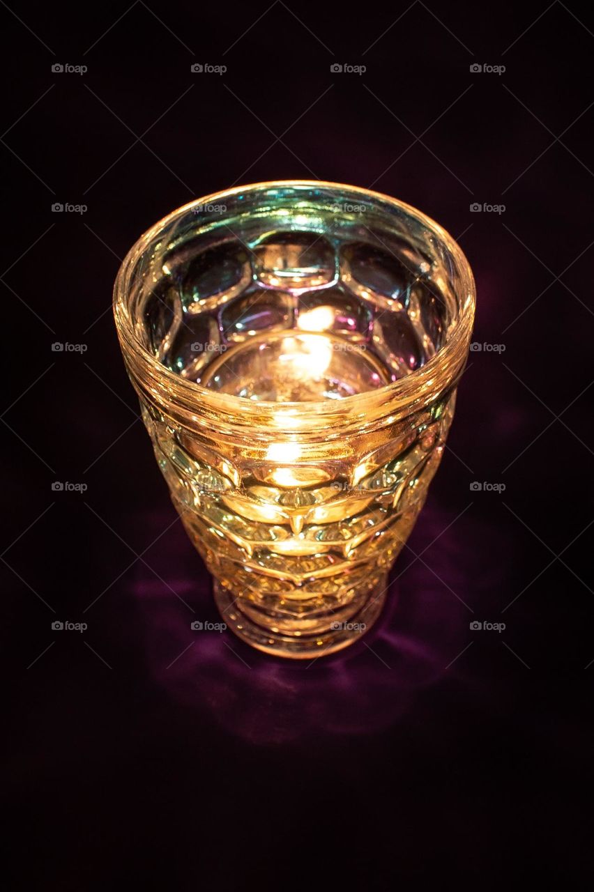 The flickering flame of a small candle through iridescent bubbled glass in the dark of night.
