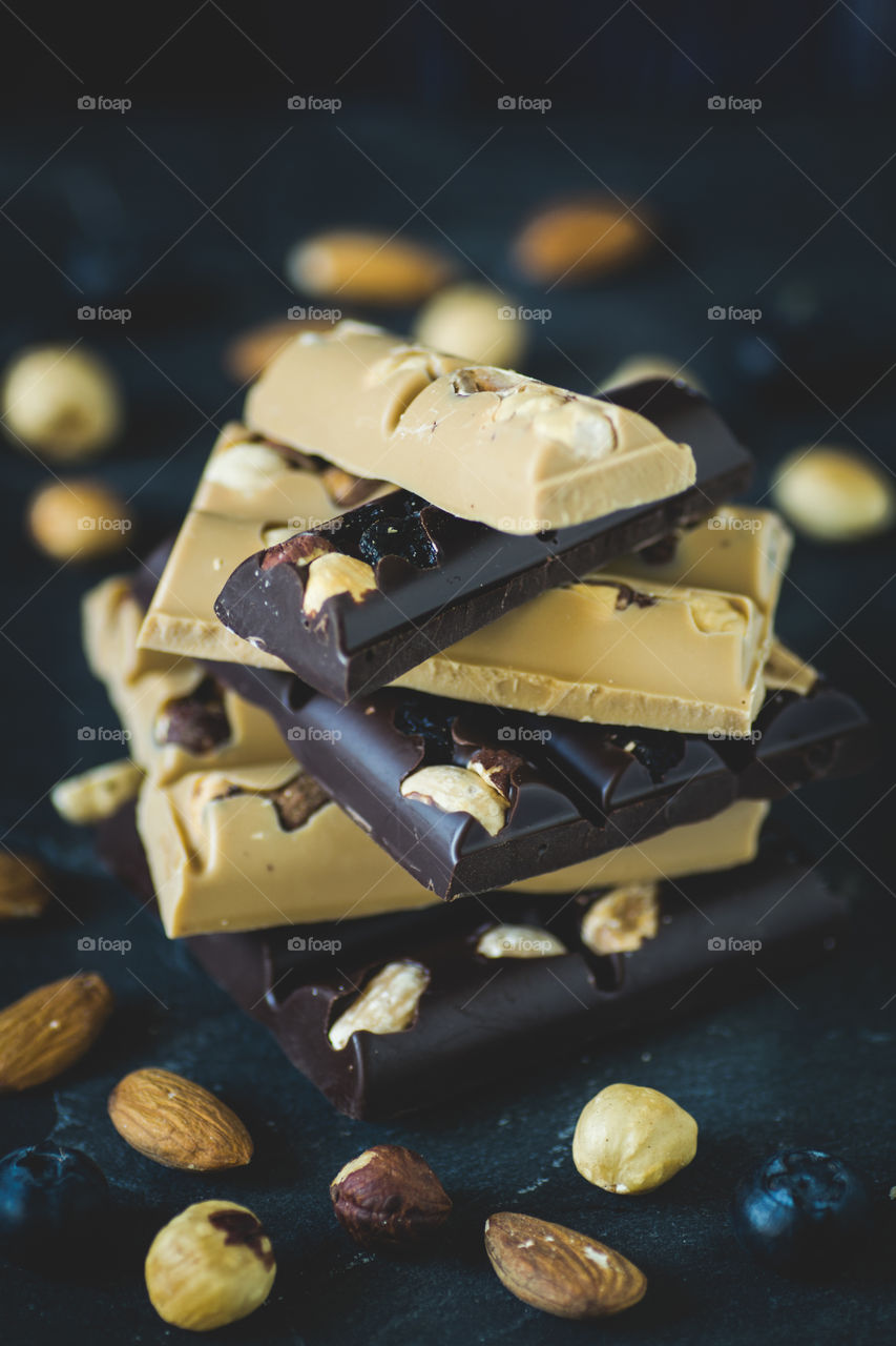 Stack of white and dark chocolate with almonds, hazelnuts and blueberries.