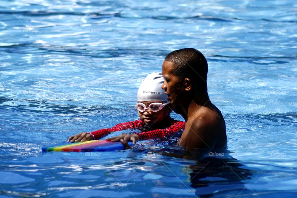 young kid learns how to swim with the help of a swimming coach