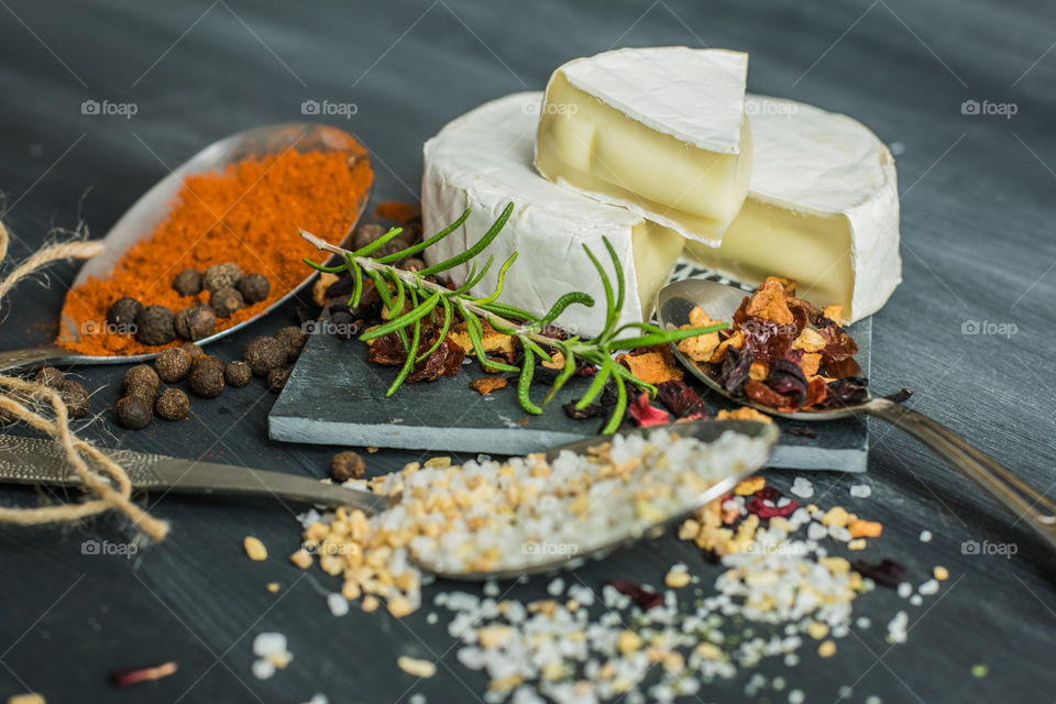 herbs, spices and camembert cheese in old, silver spoons, on a gray, stone background