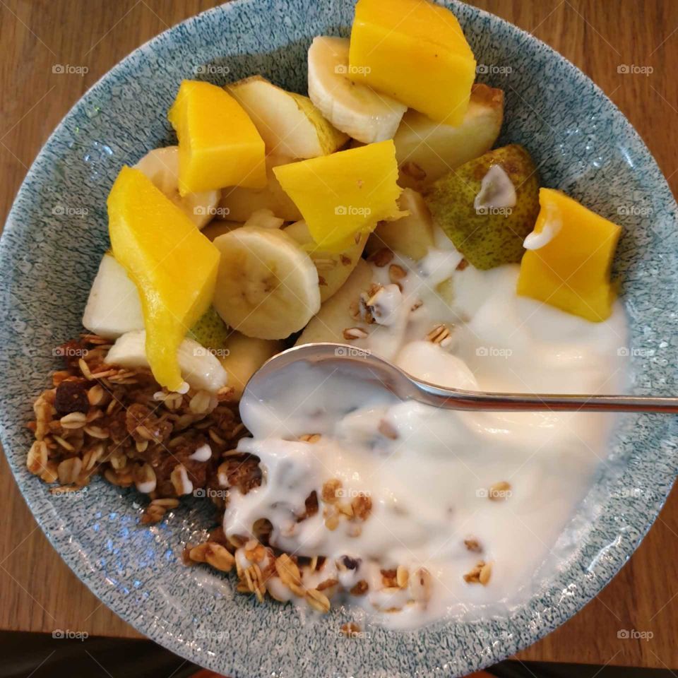 A healthy, fruity breakfast containing mango, pear, bananna, homeade granola and yogurt.