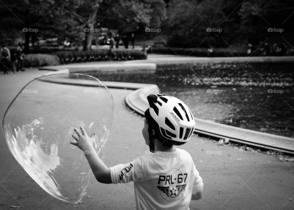 Boy Chasing Bubble In Park, Young Boy With Bubble In Central Park, Summertime Fun With Bubbles, Monochromatic Portrait Of Young Child In Central Park