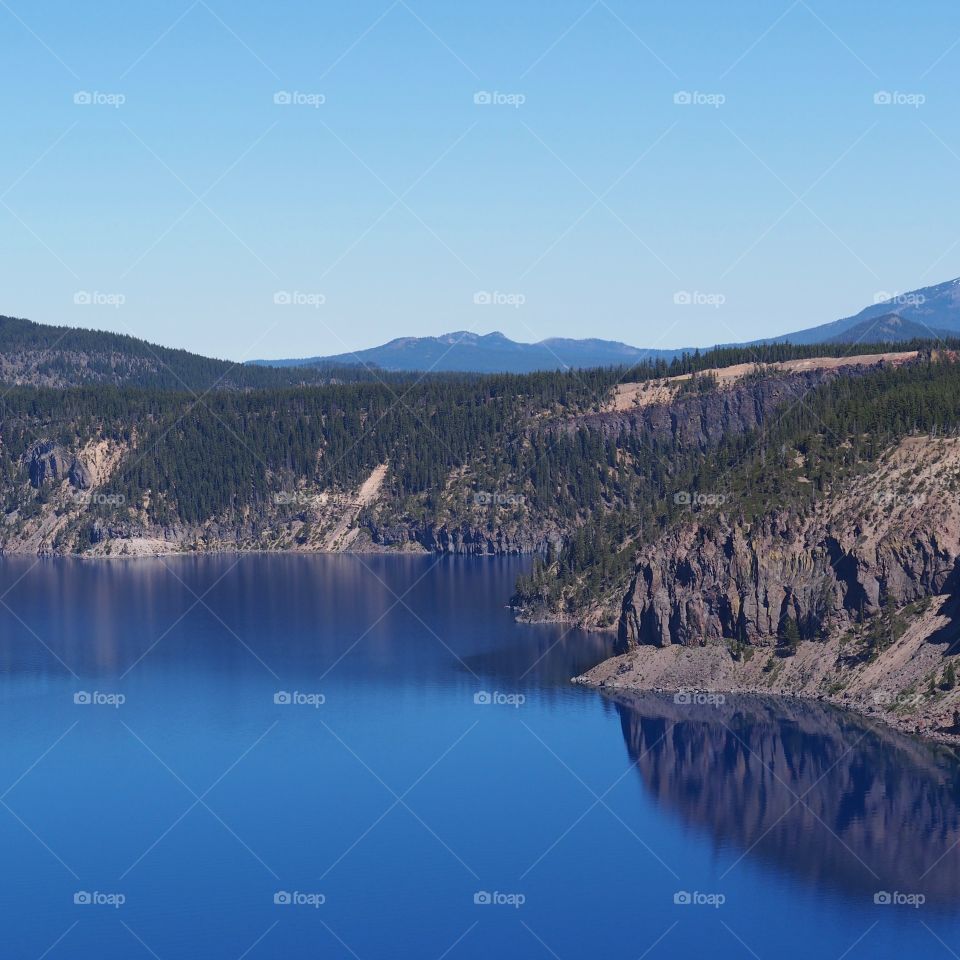 The rich blue waters of the deep Crater Lake in Southern Oregon with fir trees on the jagged rim on a beautiful sunny summer morning with clear blue skies. 