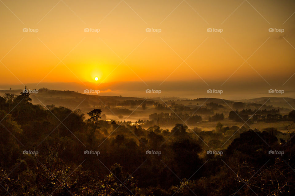 Sunrise over misty winter landscape with lakes valleys and trees. Golden yellow sunrise with fog over the water.