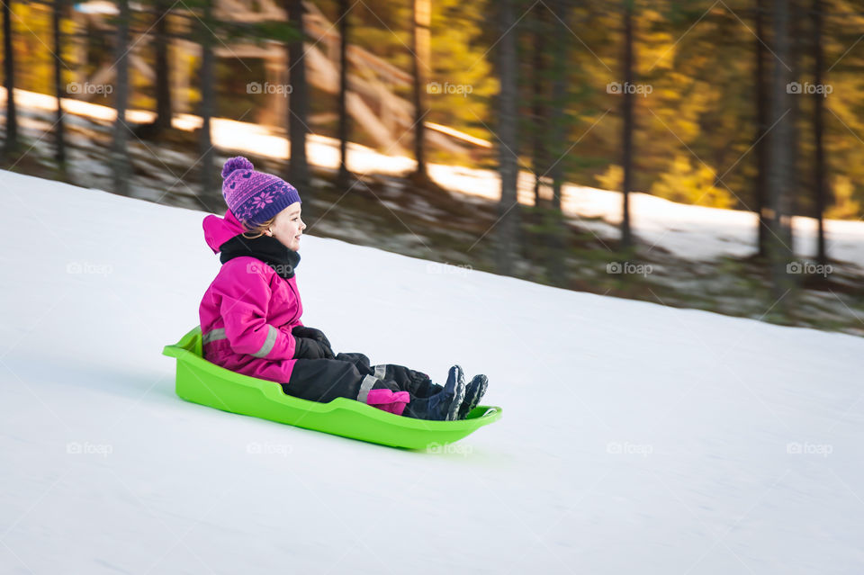 Little girl on sledge speeding downhill.