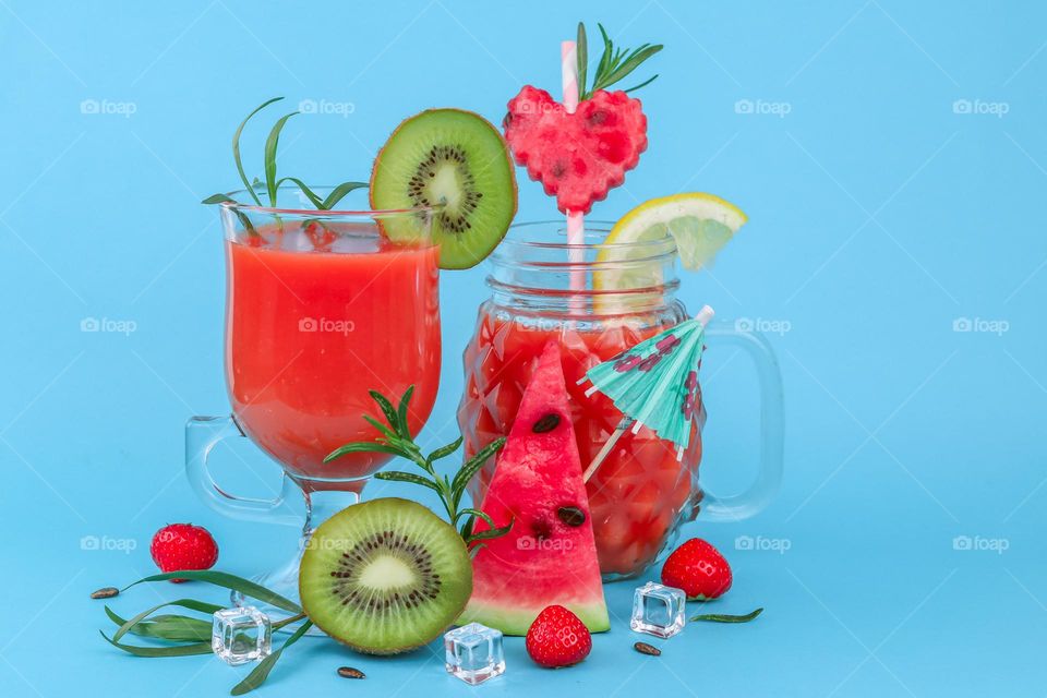 Multivitamin fruit and berry drink in glasses with fresh slices of kiwi, strawberry, watermelon, lemon and rosemary with ice on a wall background, close-up side view. Summer drinks concept.
