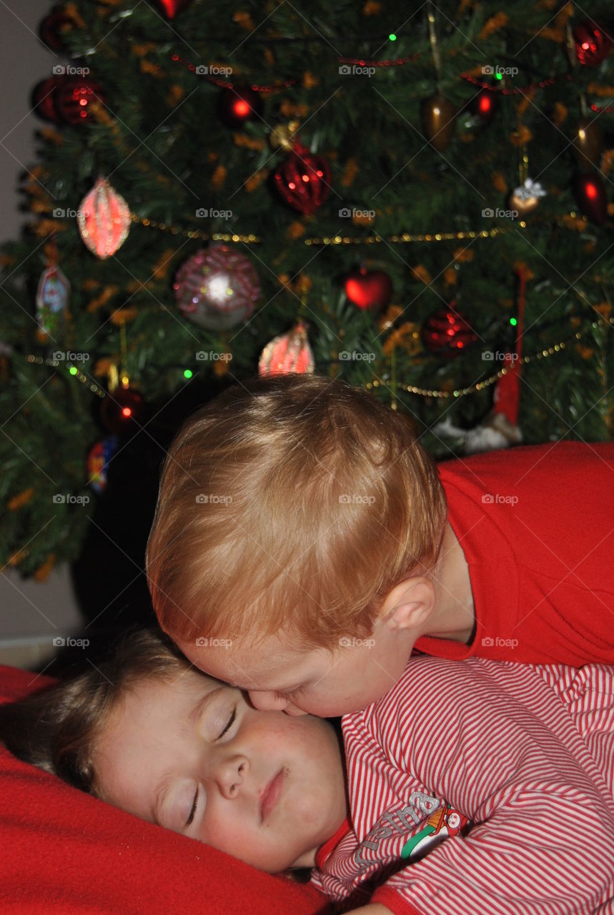 Boy kissing to his brother in front of christmas tree