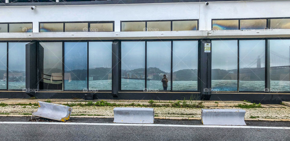 A lone individual is reflected in one of the mirrored glass windows on an overcast day