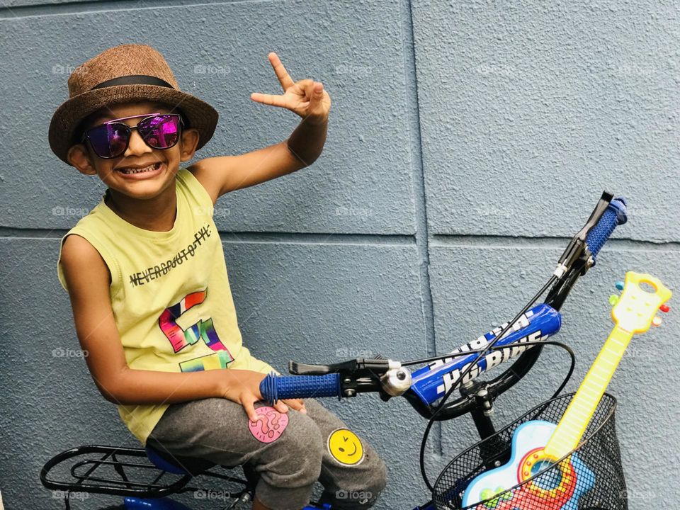 Funky and crazy style boy showing victory symbol by sitting on bicycle 