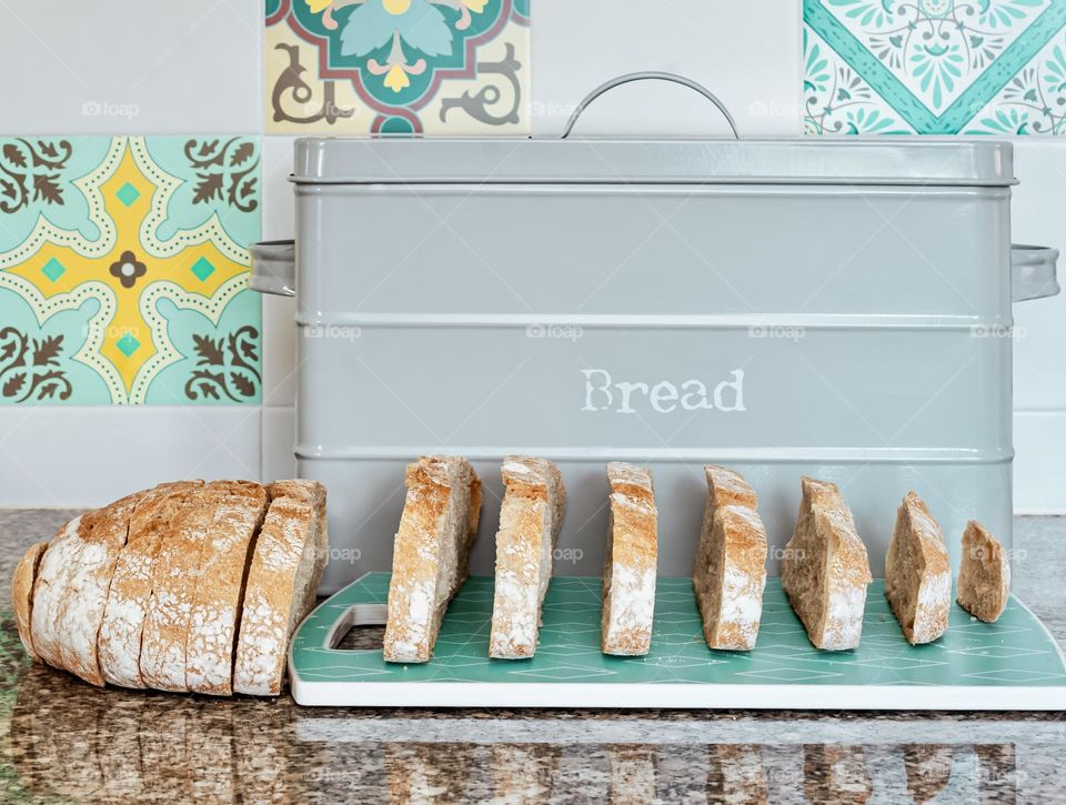 Sliced white bread spread out in front of the bread bin in a tiled kitchen