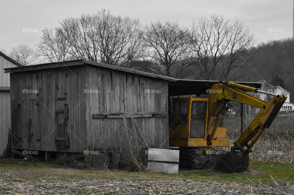 A light and subtle edit of farm equipment resting partially under cover of an old shed. 