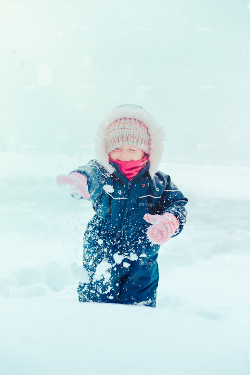 Happy little girl enjoying snow. Child playing outdoors walking through deep snow in wintertime while snow falling. Toddler is wearing dark blue snowsuit