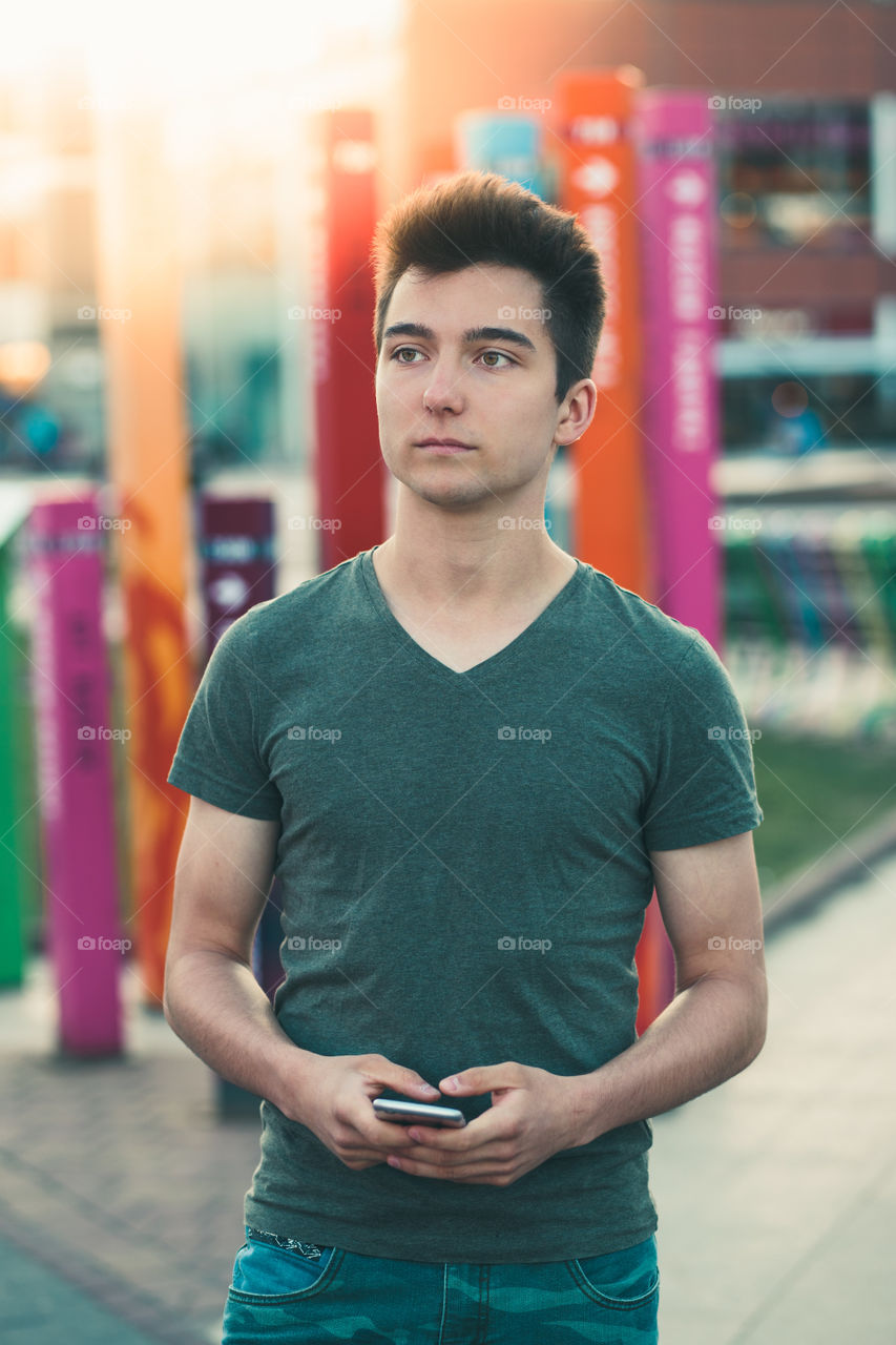 Young man holding smartphone, standing on street in center of town