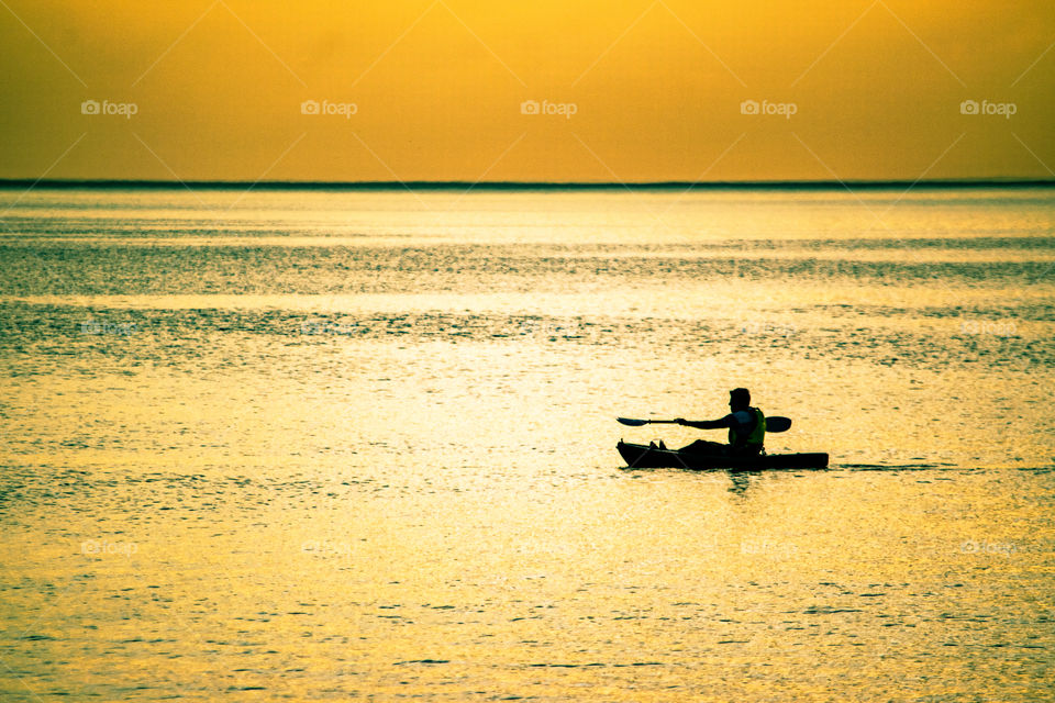 silhouette of lone kayaker on sea as sun begins to set casting a golden glow across the sea and sky