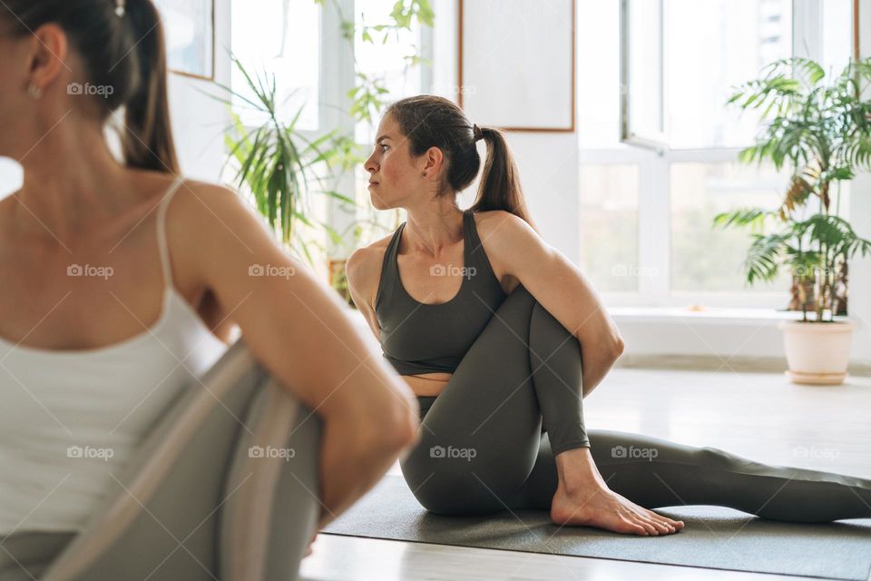 Young fit women practice yoga doing asana in bright yoga studio. Yoga ticher practices with student in yoga class
