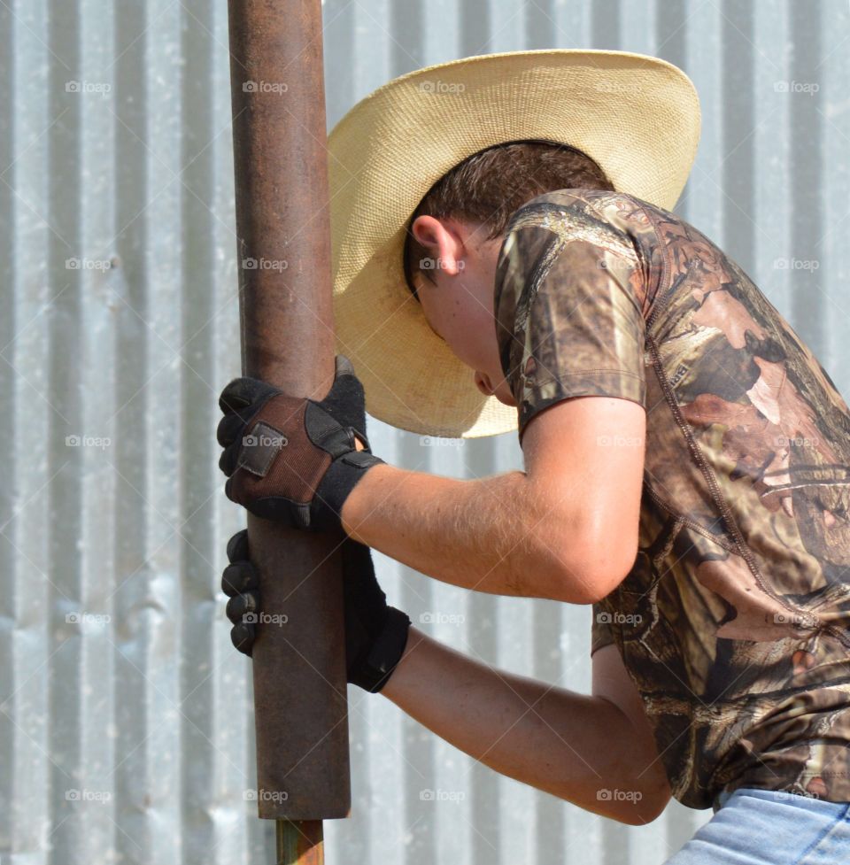 Young cowboy driving fence post into the ground by hand 