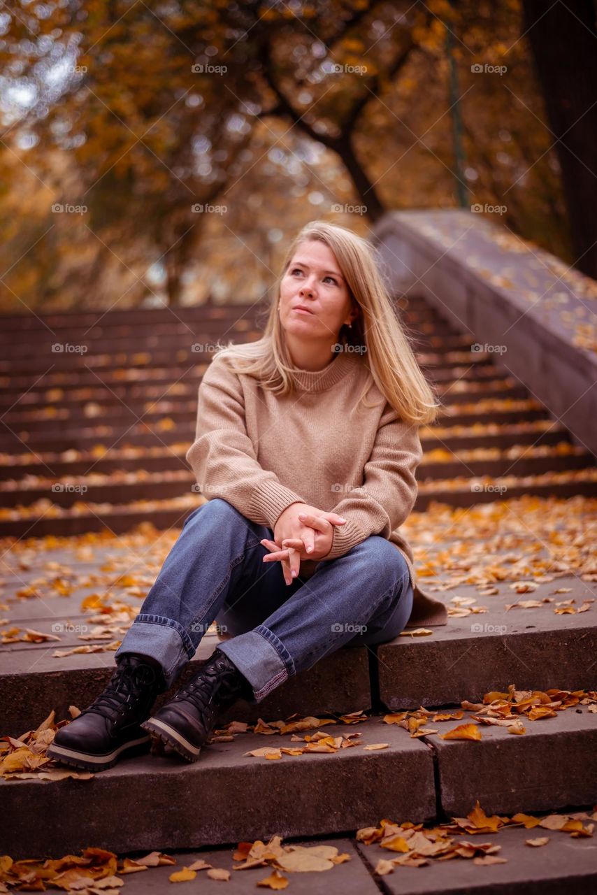 Autumn season city square with fallen leaves a young girl sits on the steps