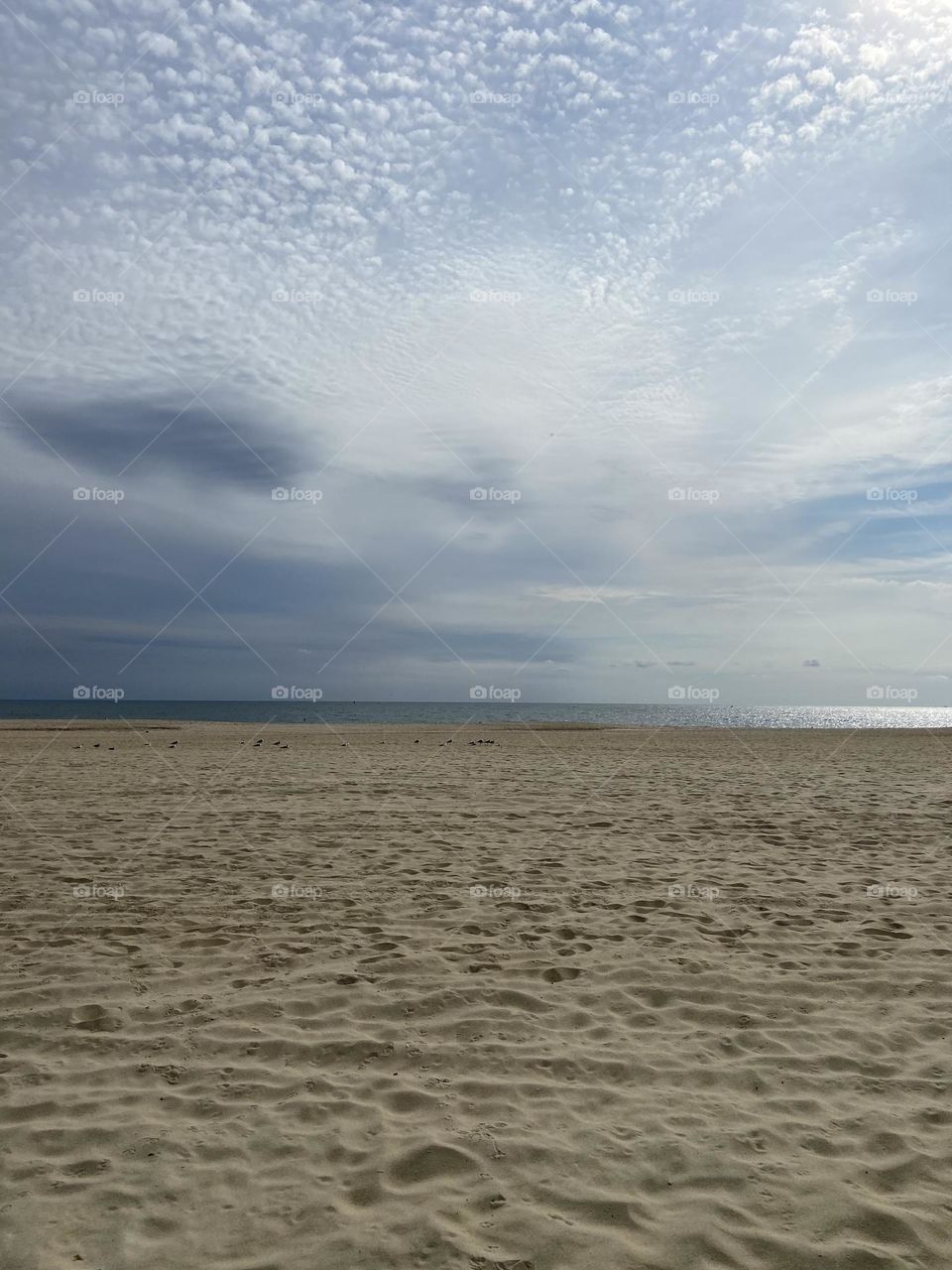 A cloud-filled sky above a sliver of sparkling blue ocean and a sandy beach marked with footprints from beach-goers past. The beach is pretty deserted on this recent September morning, except for some seagulls. The quiet beauty is breathtaking.
