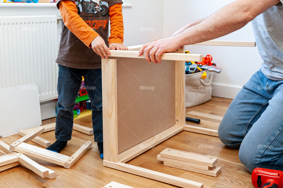 Parent with child assembling flat pack desk furniture for child's bedroom.