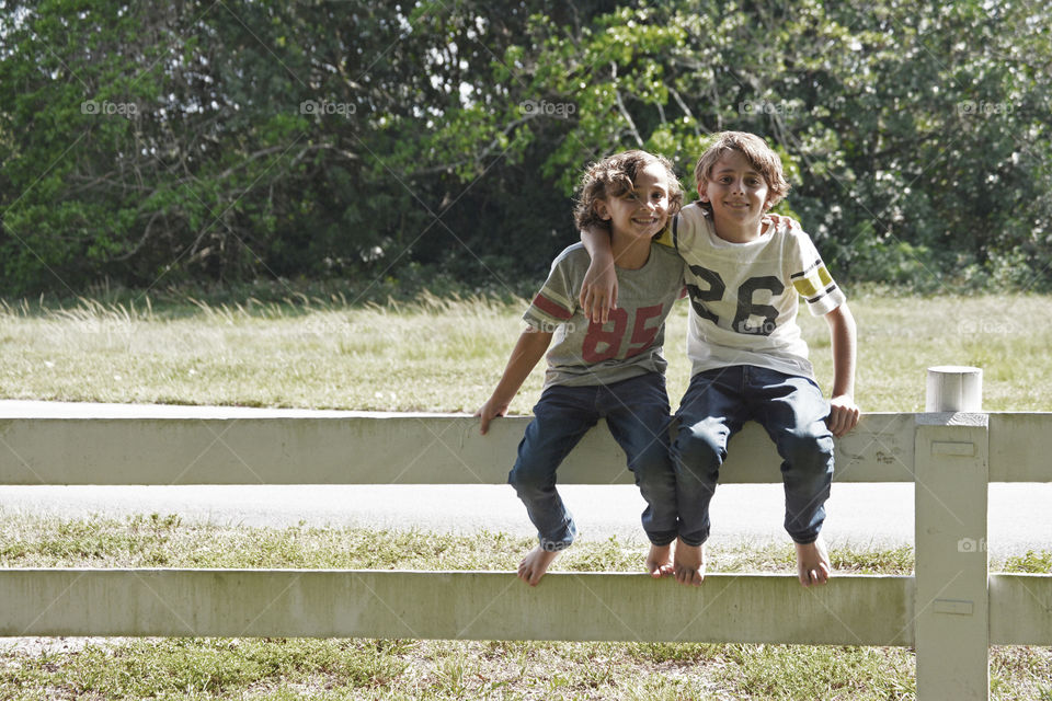 Two brothers sitting on wooden fence