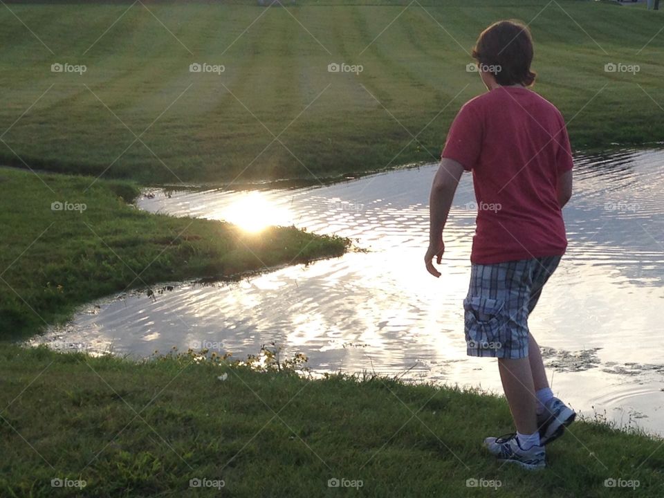 Teenager walking next to a pond in the evening.