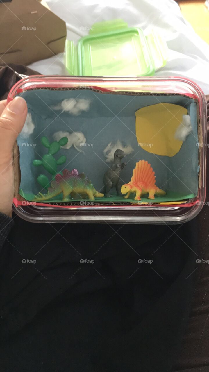 Cute dinosaur diorama out of paper and plastic dinosaurs in a glass storage container