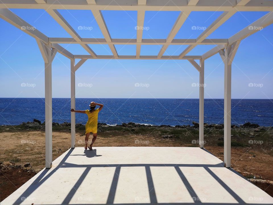 woman from behind dressed in yellow looks at the calm sea from the white porch